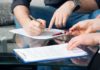 Two people reviewing and signing documents on a glass table