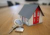 a small red and white model house sitting on a table next to a key on a ring